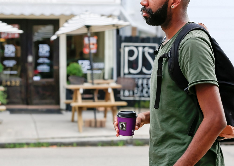 Person walking in front of a PJ's location holding a PJ's coffee cup.